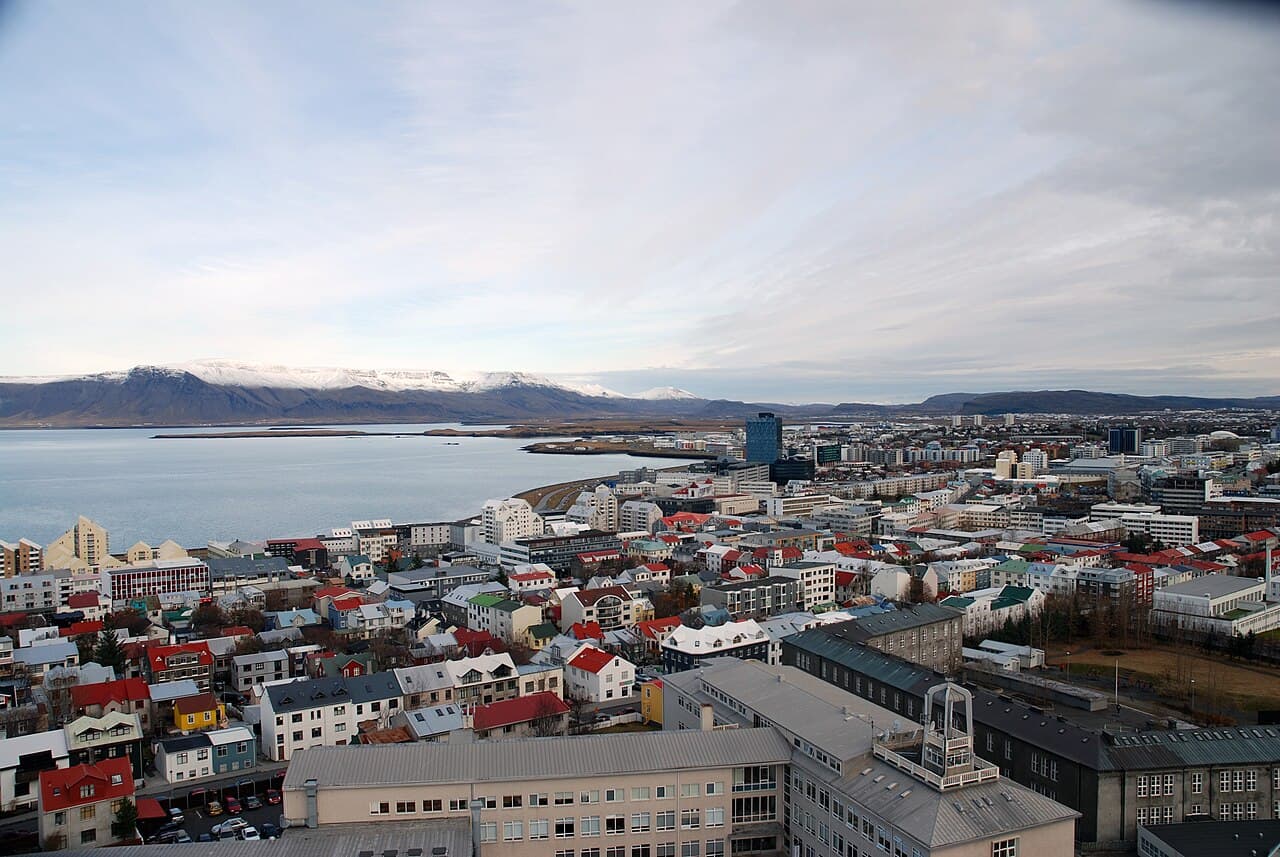 Reykjavík rooftops and bay seen from above, with snow-capped Mount Esja across the water